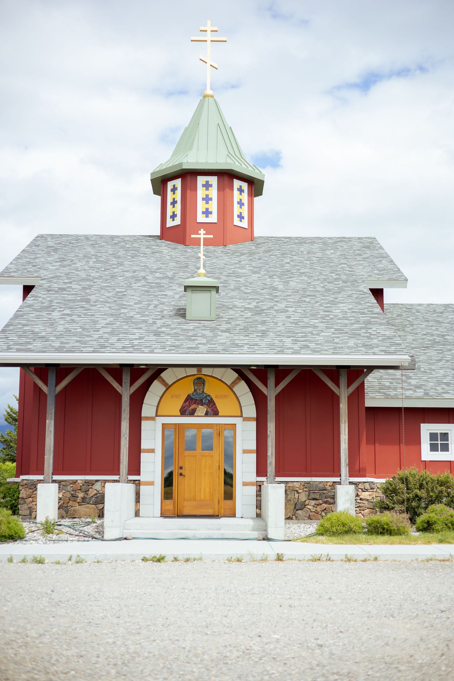 Modern red church building with white trim and a copper steeple against blue sky.
