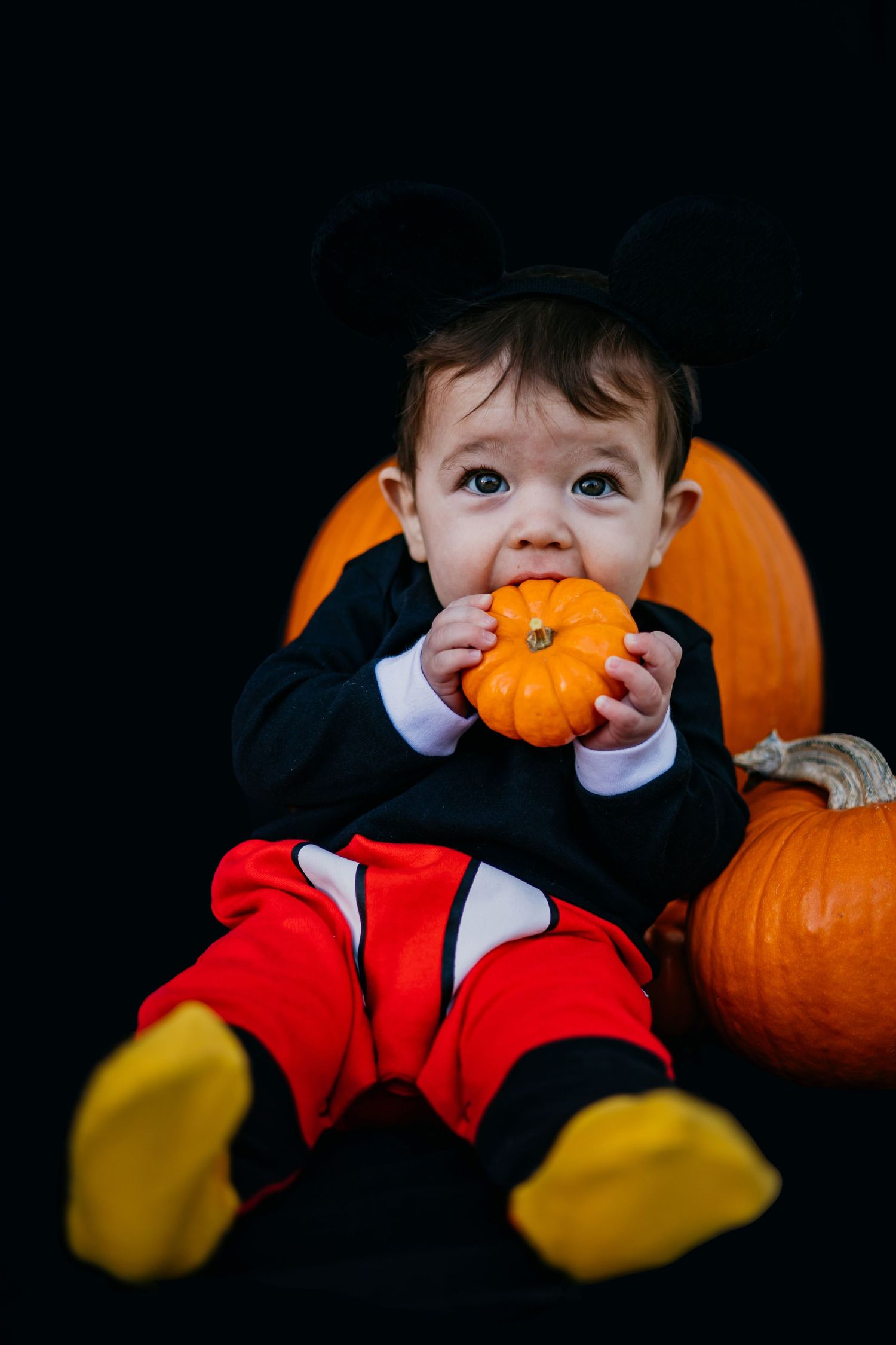 Mickey Mouse costume with yellow gloves and pumpkins in dark setting.