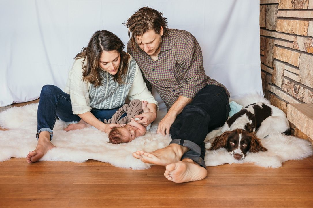 Family and dog relaxing together on cozy white blankets against wooden wall.