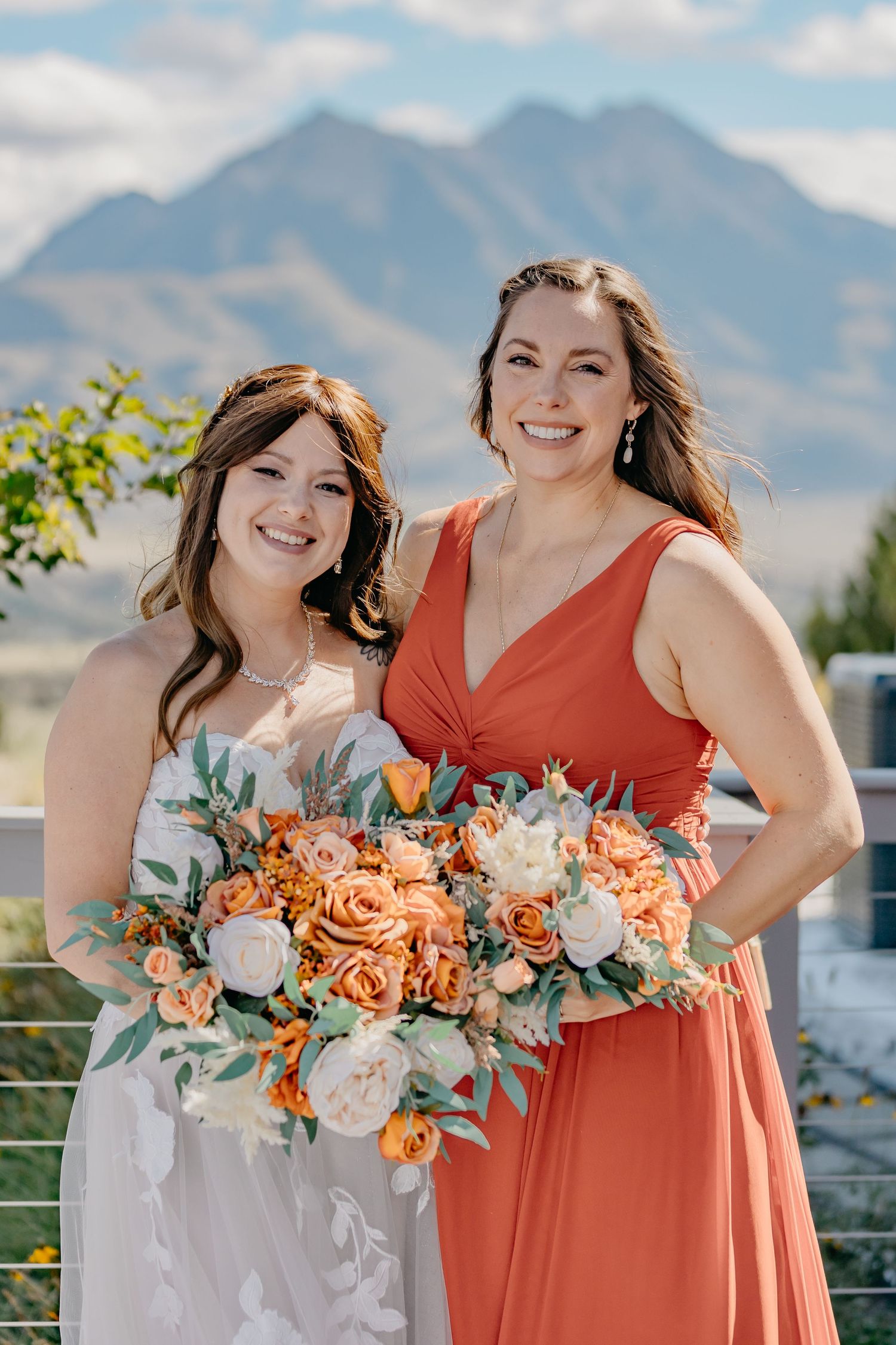 Bridesmaids in coral and white dresses holding floral bouquets with mountains in background.
