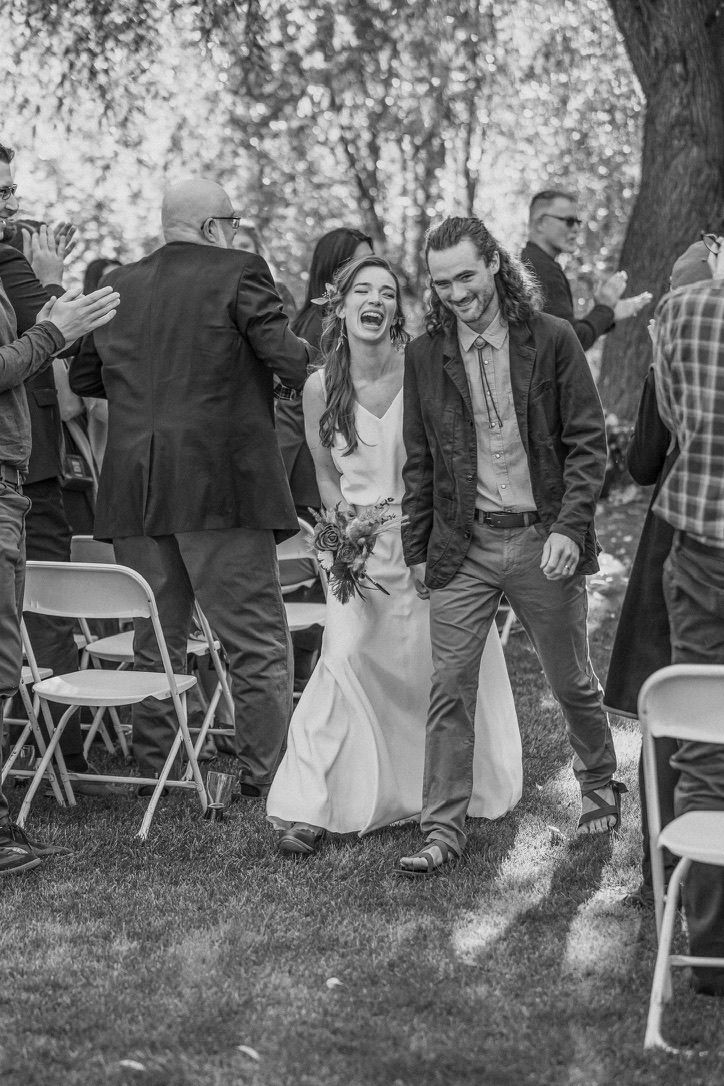 A joyful wedding couple walks down the aisle while guests applaud at an outdoor ceremony.