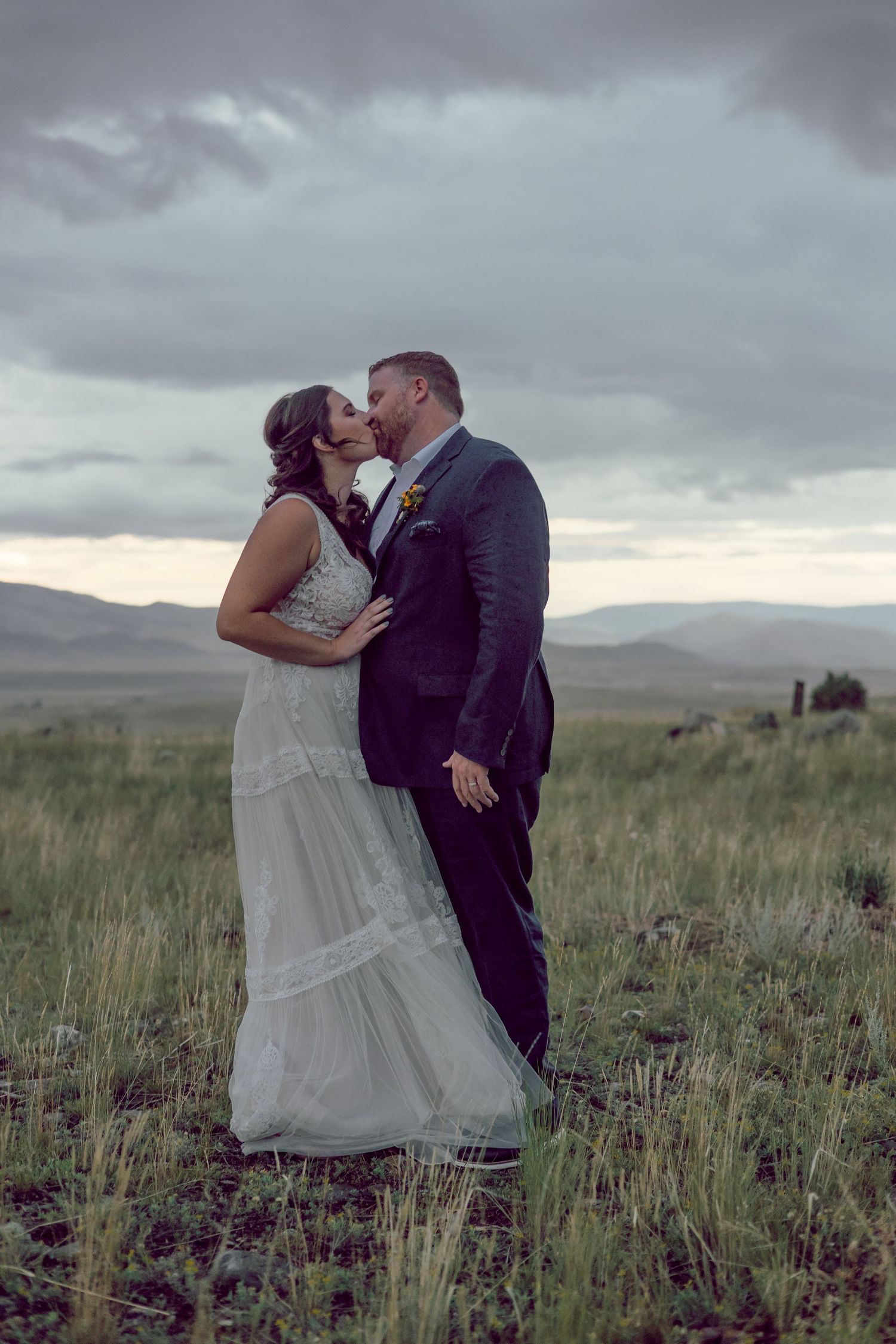 Couple shares intimate moment in field under dramatic stormy sky.