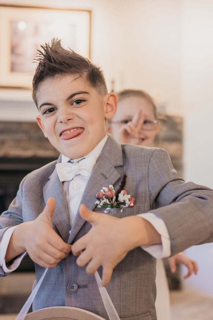 Young ring bearer in grey suit making silly faces at wedding.