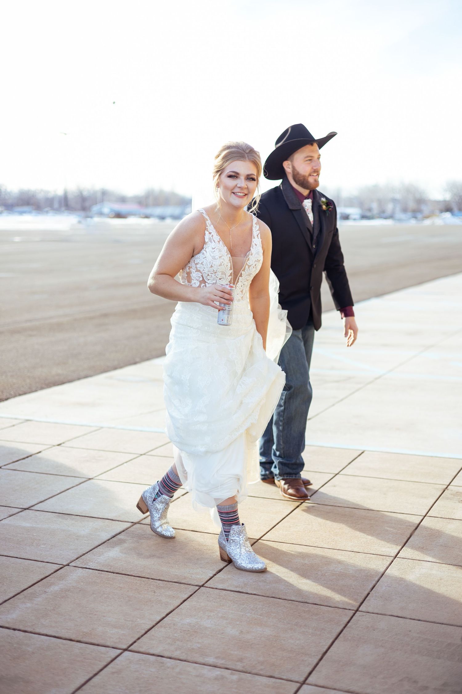 Bride in white dress and sneakers poses playfully on concrete patio.