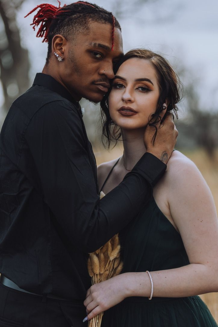 A romantic couple in formal black attire shares an intimate moment during a moody photoshoot.
