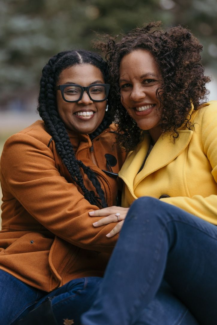 Two friends in bright yellow and brown jackets share joyful laughter outdoors.