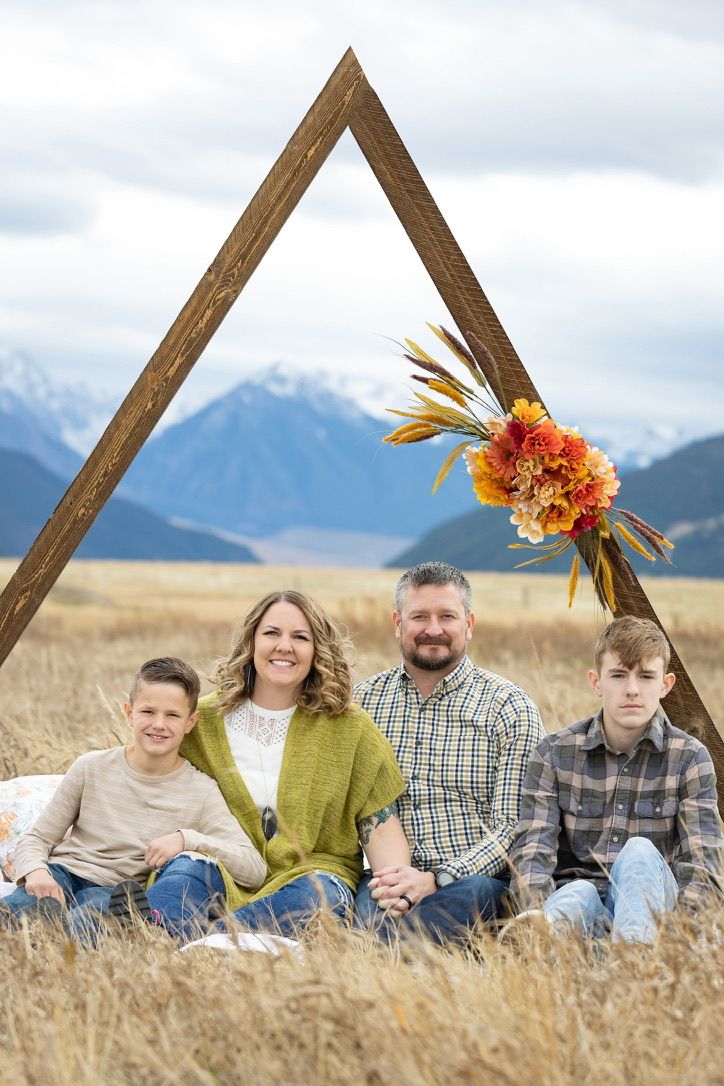 Family portrait in golden field with mountain backdrop and wooden triangle frame.