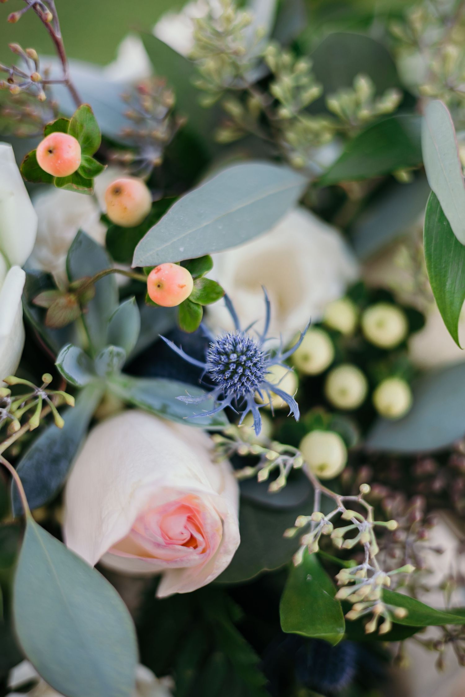 Detailed view of wedding bouquet with pale pink roses, blue thistle, and white berries.