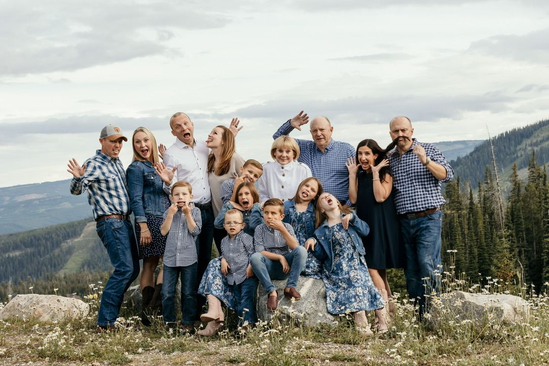 Large family group poses together on mountain overlook with scenic valley view.