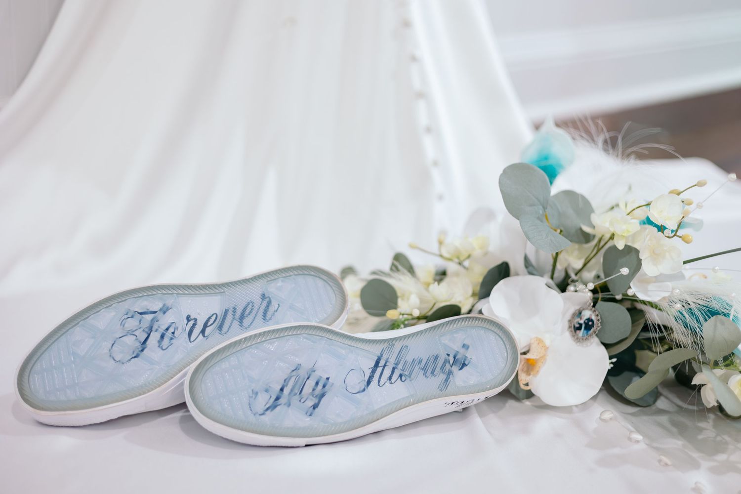 Wedding shoes with 'Forever' text and floral decorations arranged on light background.