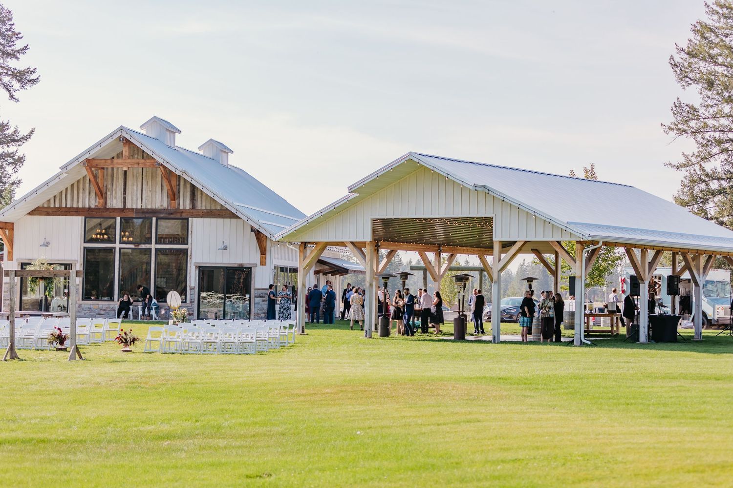 Panoramic view of white barn wedding venue buildings nestled against mountain backdrop.