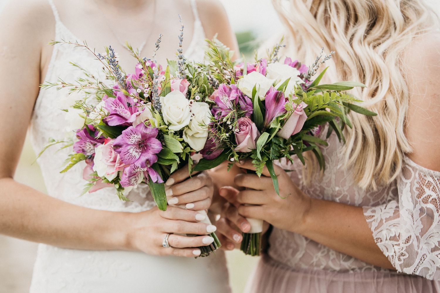 A beautiful pink and white wedding bouquet with mixed flowers and greenery held by hands in lace.