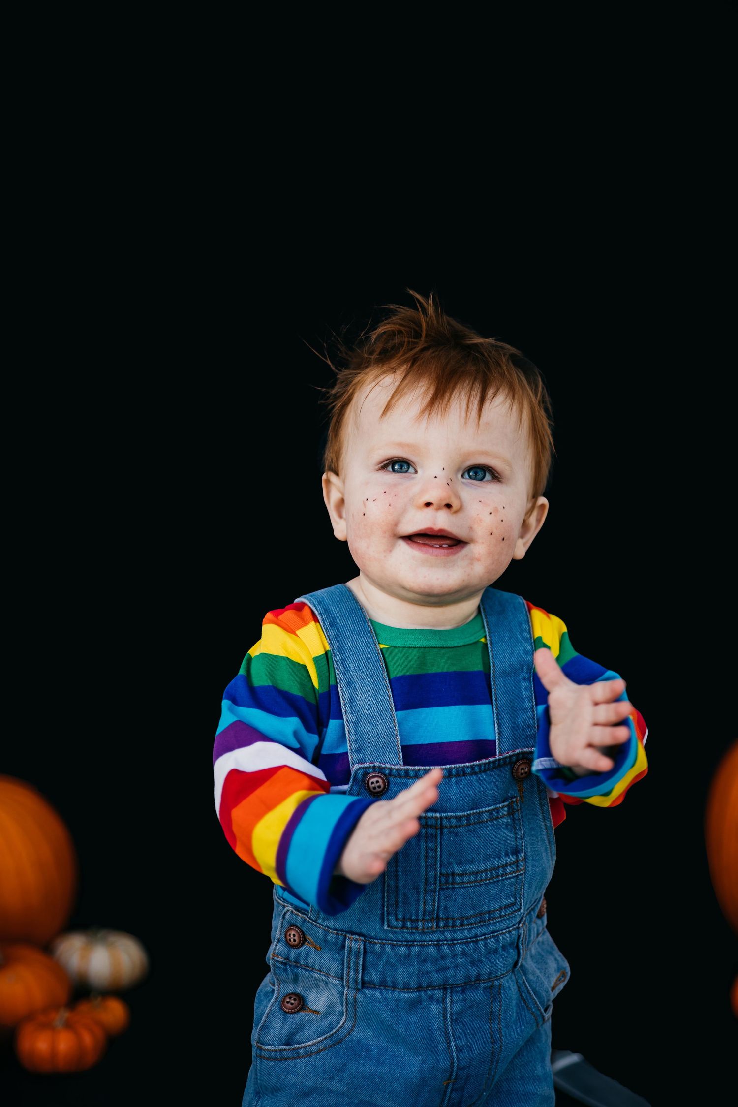 Rainbow striped shirt and denim overalls outfit against dark backdrop.