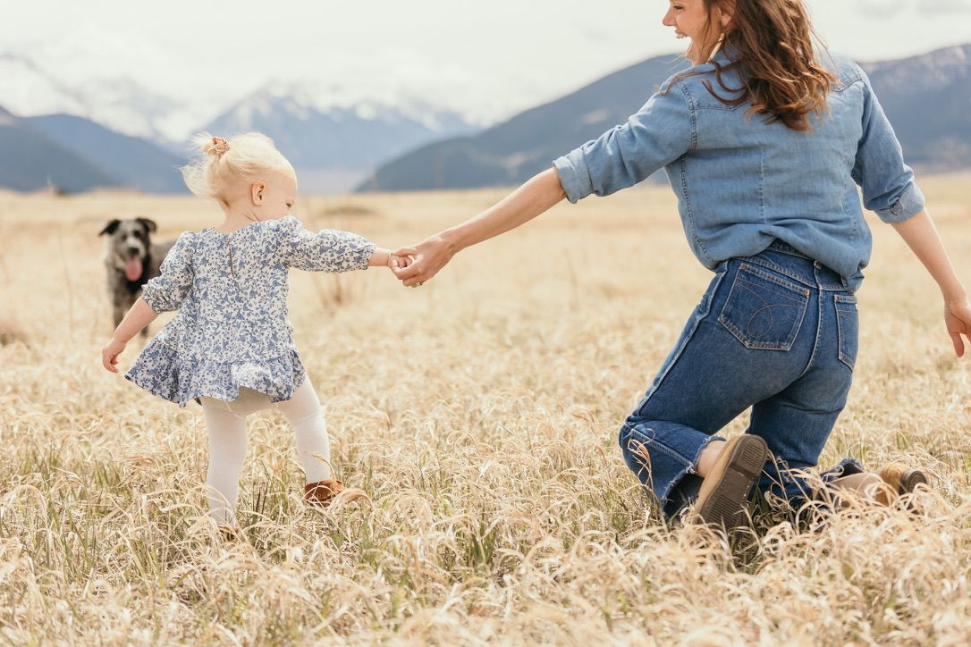 People running and playing in a golden wheat field with mountains in background.