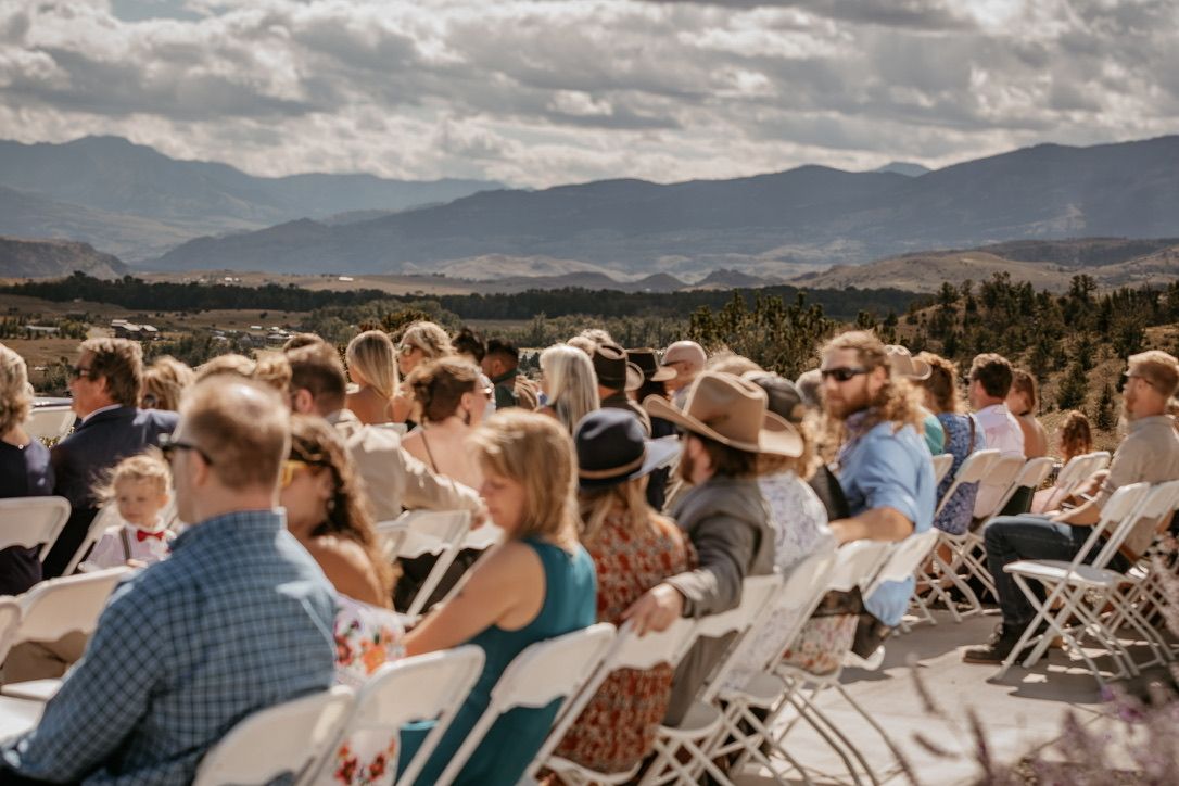 Wedding guests seated in white chairs overlooking a scenic mountain landscape.
