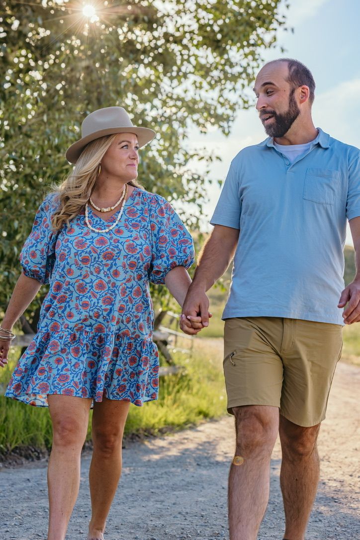 Couple walking together on dirt path during sunset with trees in background.