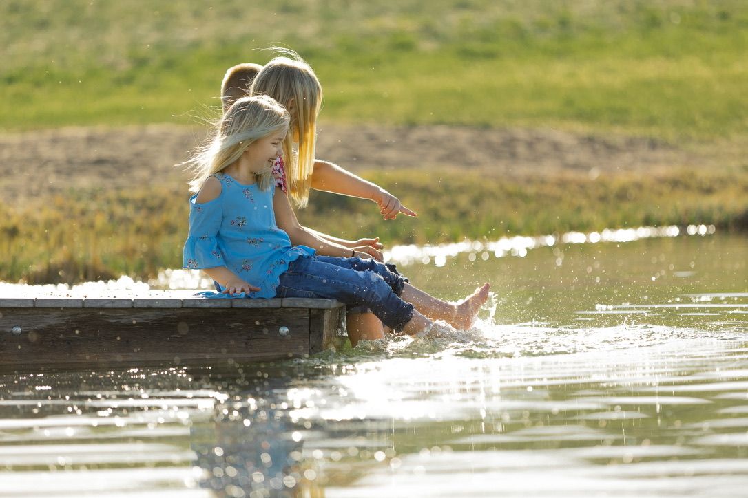 Children sitting on dock splashing feet in water during golden sunset.