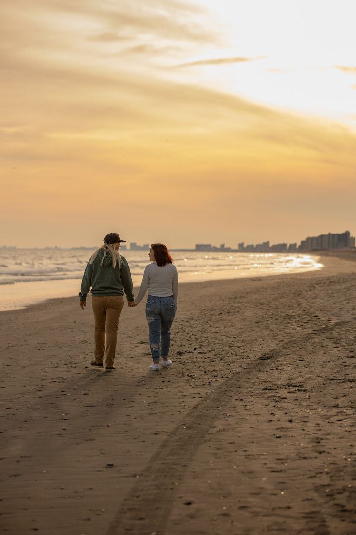 Couple walking hand in hand on beach during golden sunset.