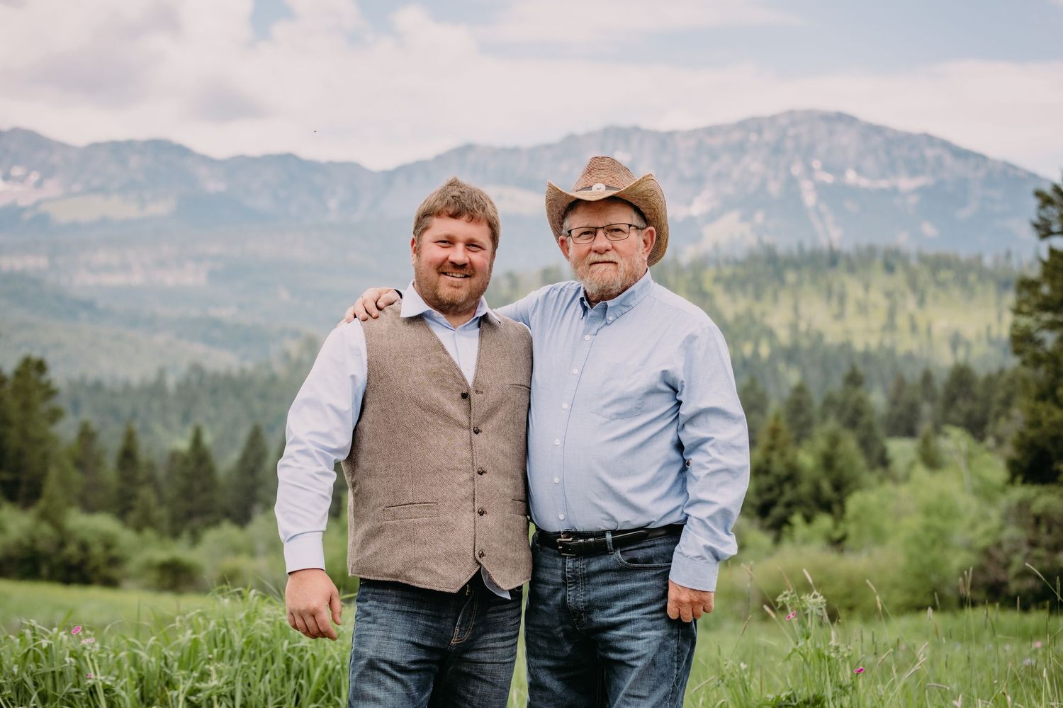 Outdoor portrait session against scenic mountain backdrop with brown vest and blue shirt attire.