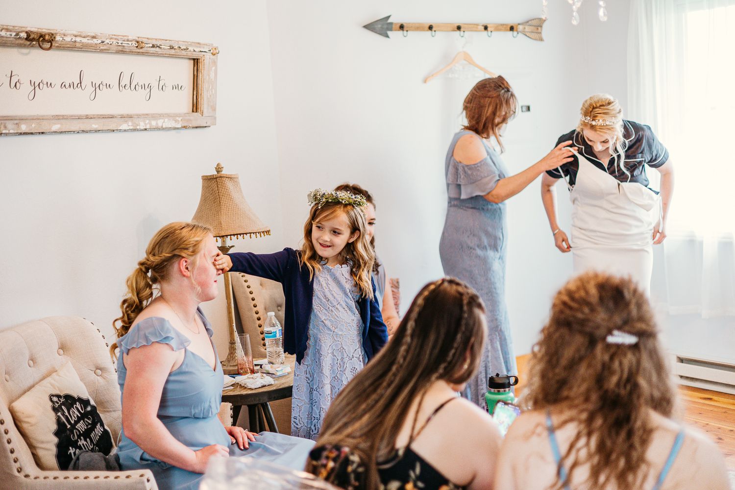 Bridal party getting ready in light-filled room with rustic decor and arrow wall art.