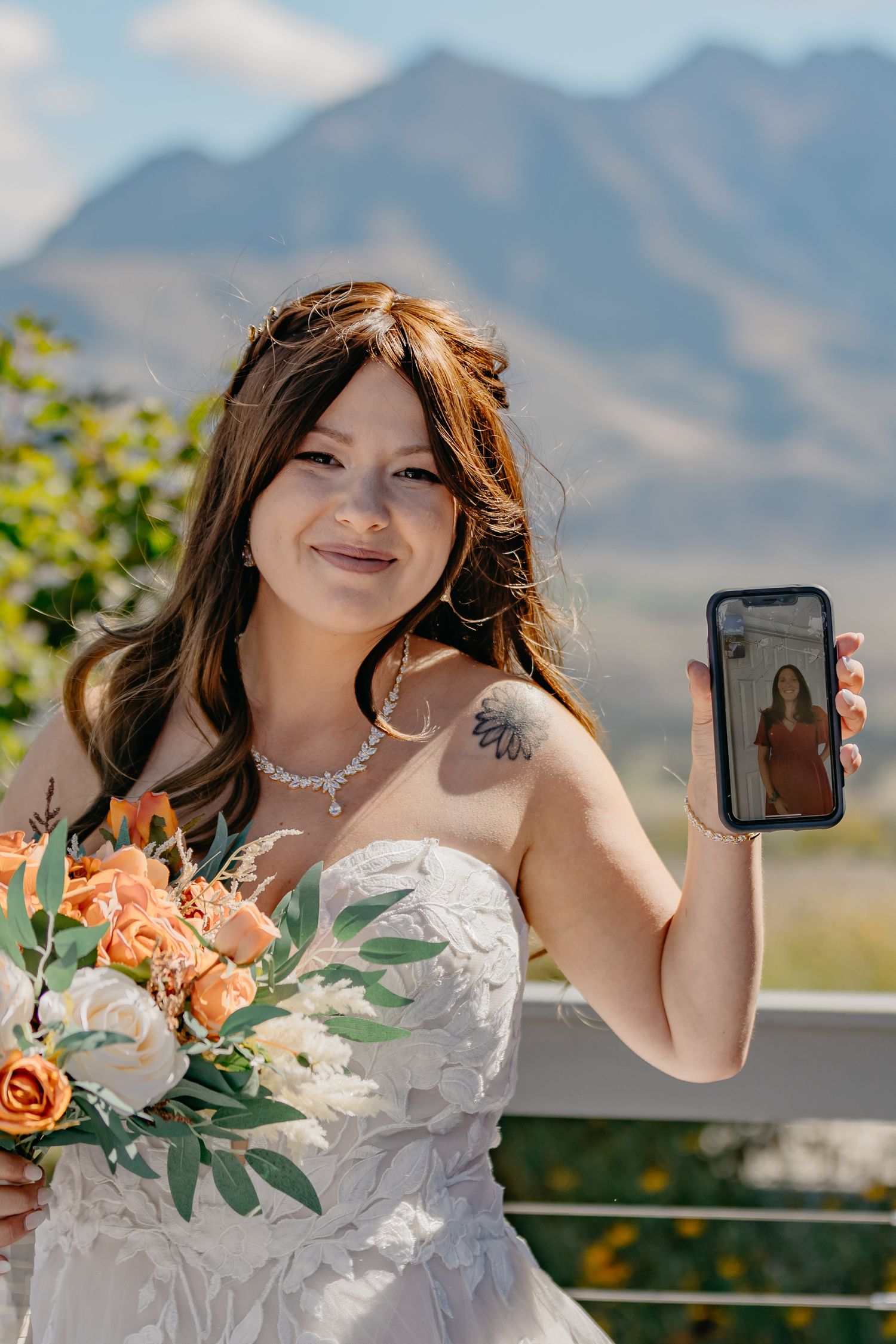 Bride holding bouquet of orange and white flowers against mountain landscape.
