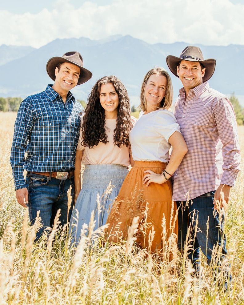 Group wearing western attire poses in field with mountain backdrop.