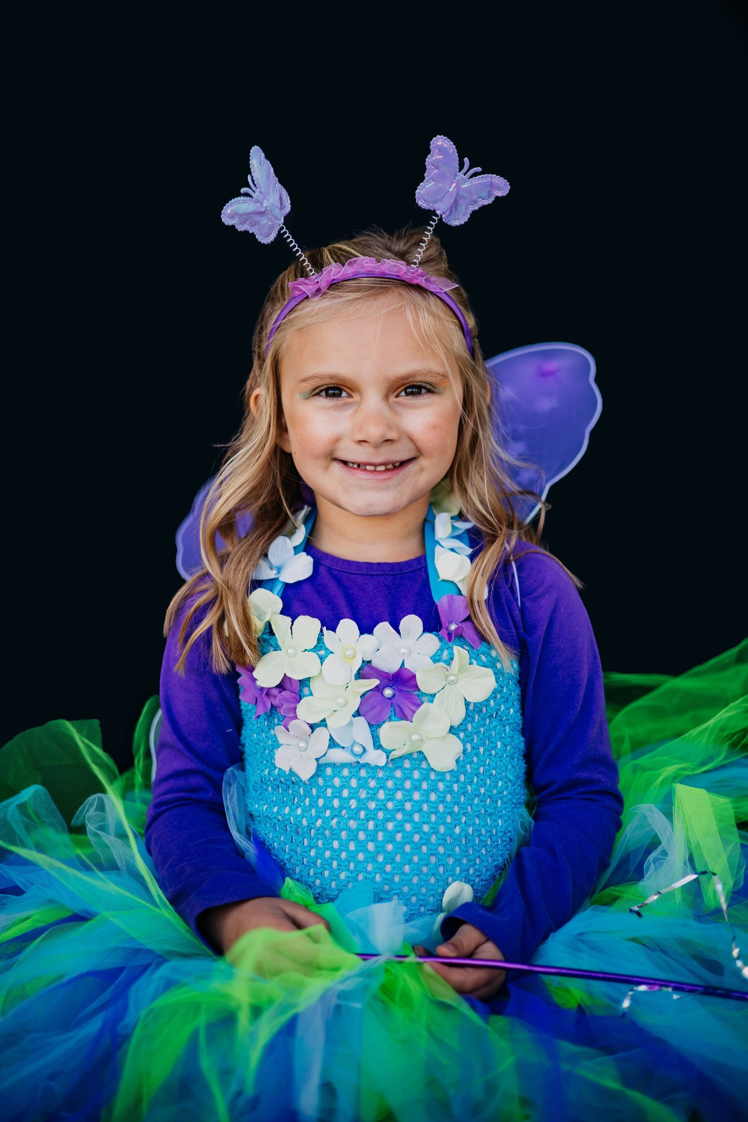 Bright butterfly costume with blue and green tulle tutu against black background.