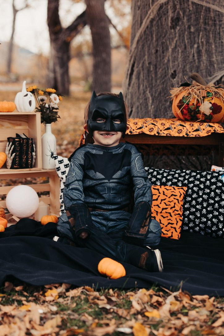Halloween themed photo session with Batman costume and orange decorations on dark backdrop.