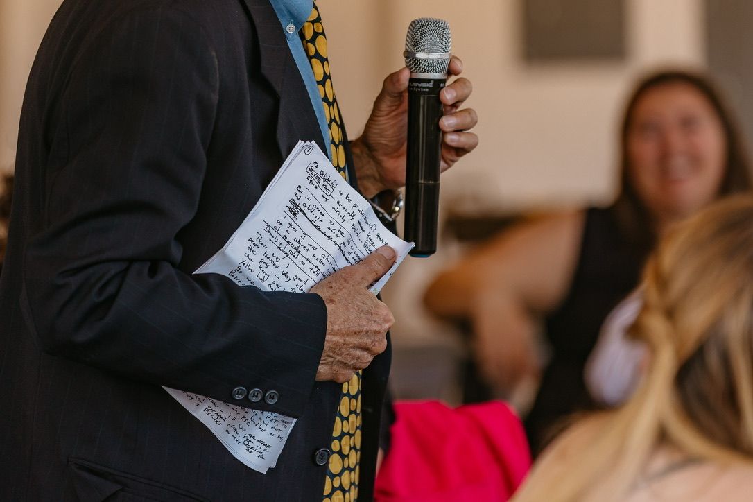 Wedding guest holding a microphone and paper while giving a speech at reception.
