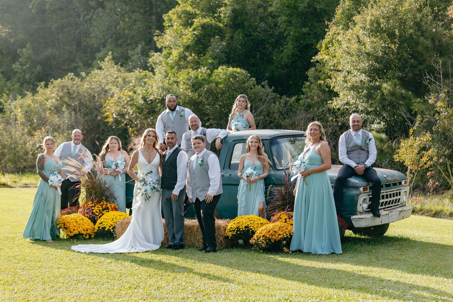 Wedding party gathers outdoors with yellow mums and autumn foliage in the background.