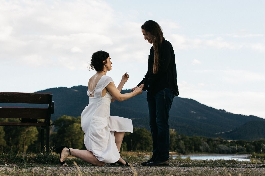 A romantic proposal scene with one person kneeling before another against a mountain backdrop.