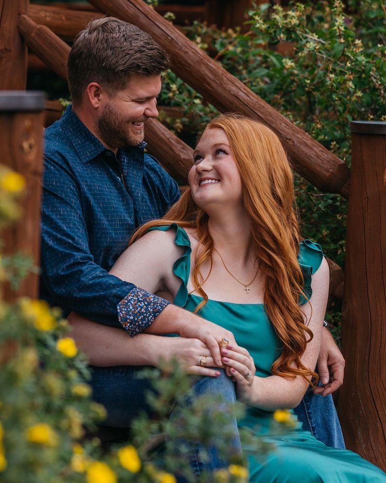 Couple sharing intimate moment on wooden deck surrounded by flowers.