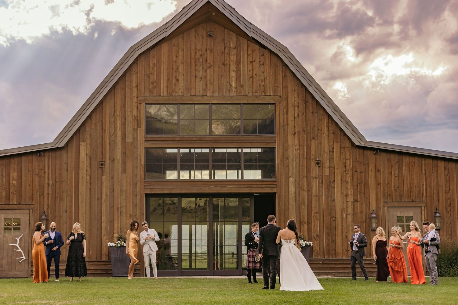A rustic barn wedding venue exterior with wooden walls and large windows at sunset.