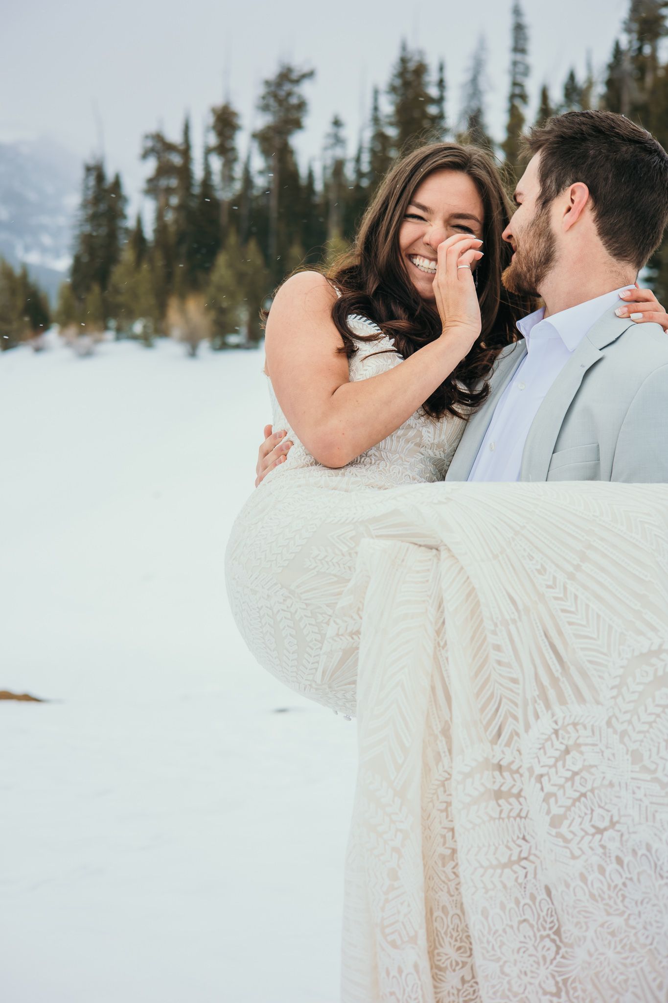 A romantic winter wedding photo shoot in a snowy forest with evergreen trees in the background.