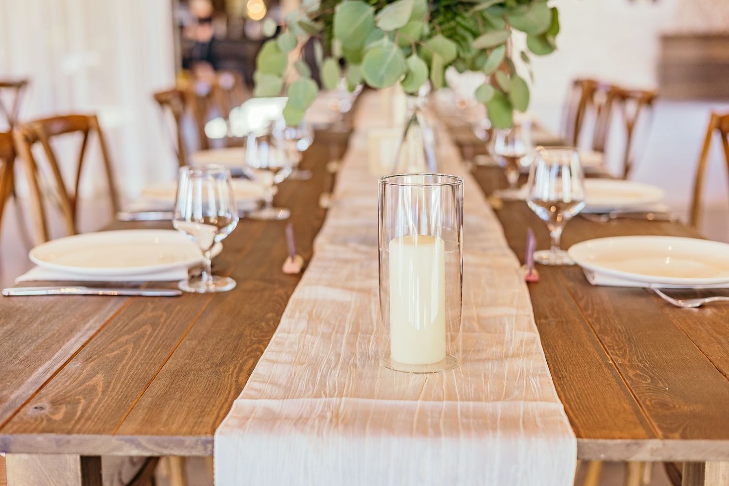 Long wooden tables with white runners and place settings in an elegant rustic dining setup.