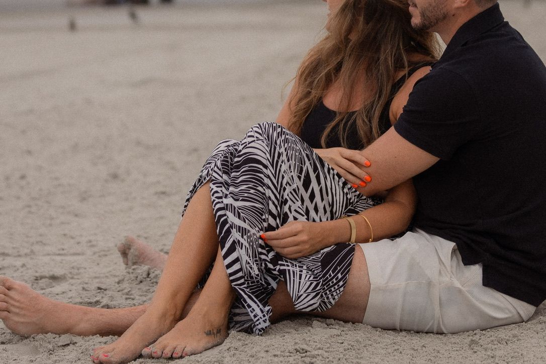 Couple sitting close together on beach wearing black and zebra print clothing.