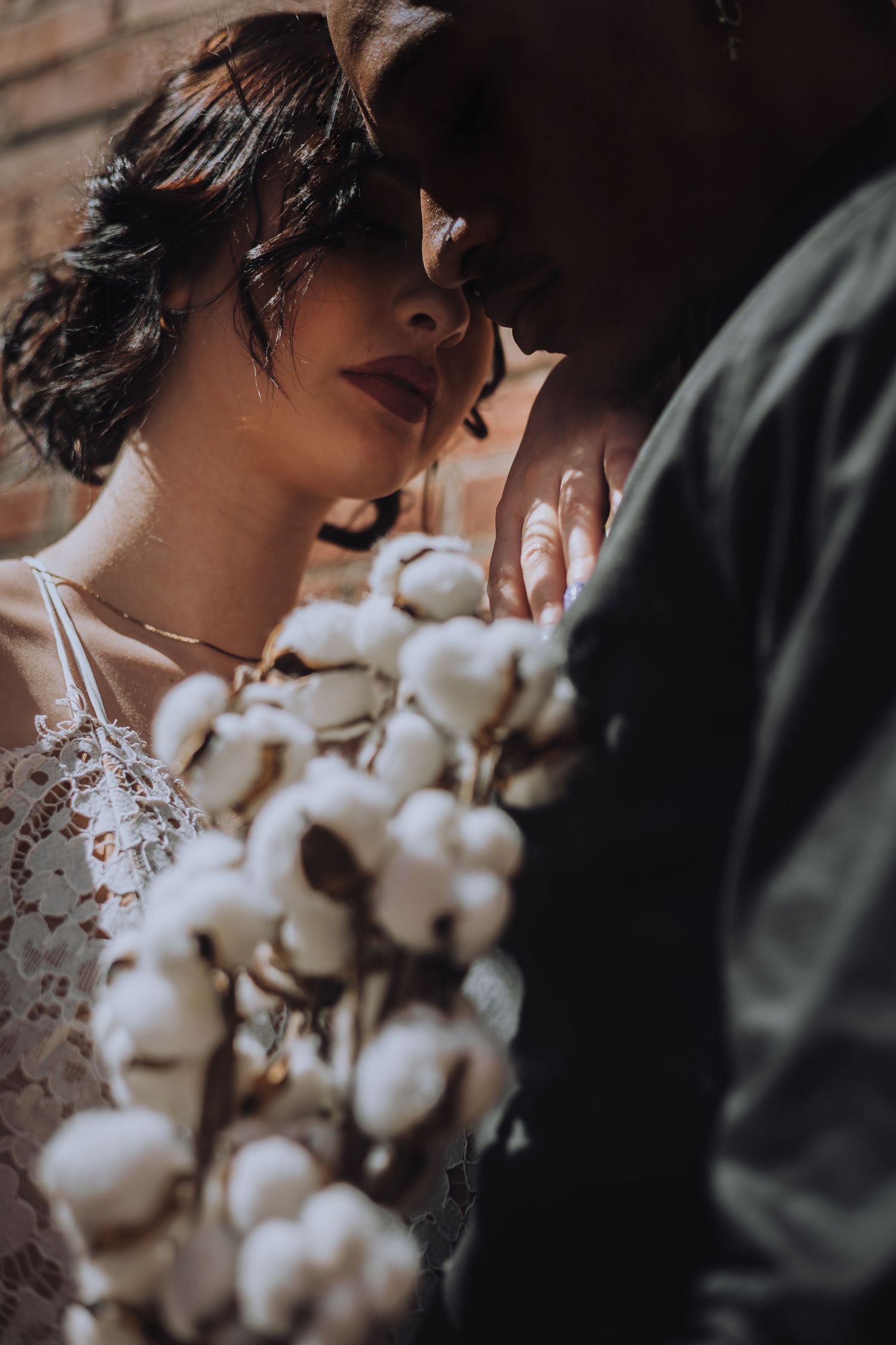 Romantic wedding portrait with cotton bouquet and intimate close-up against dark background.