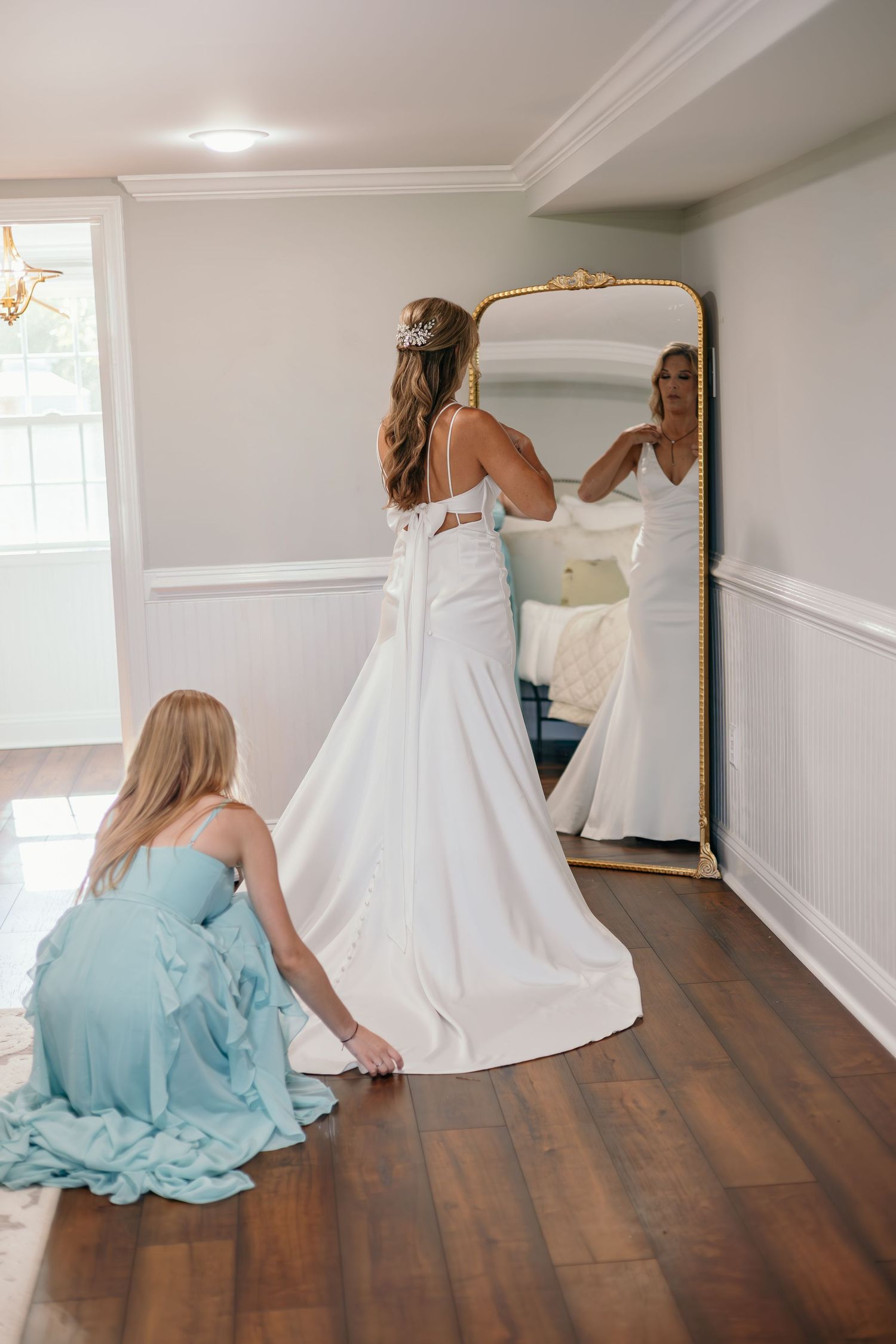 A white wedding dress is being fitted in a room with hardwood floors and mint green bridesmaid dresses.