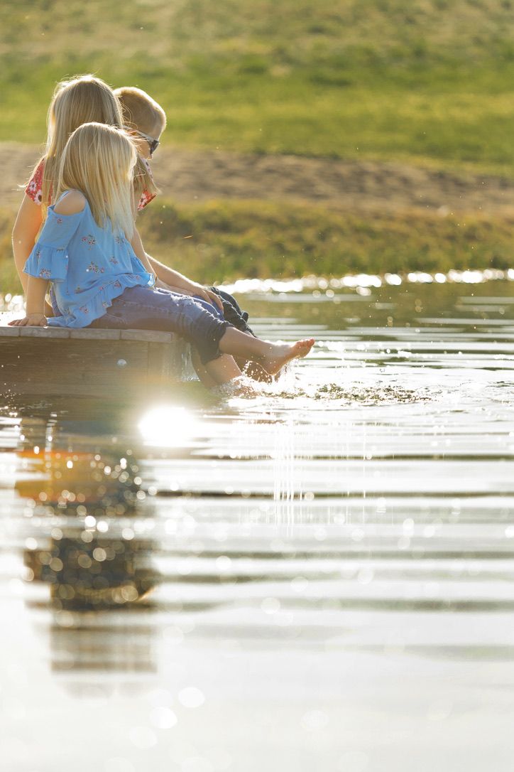 People sitting by water's edge with sun creating sparkles on the surface.