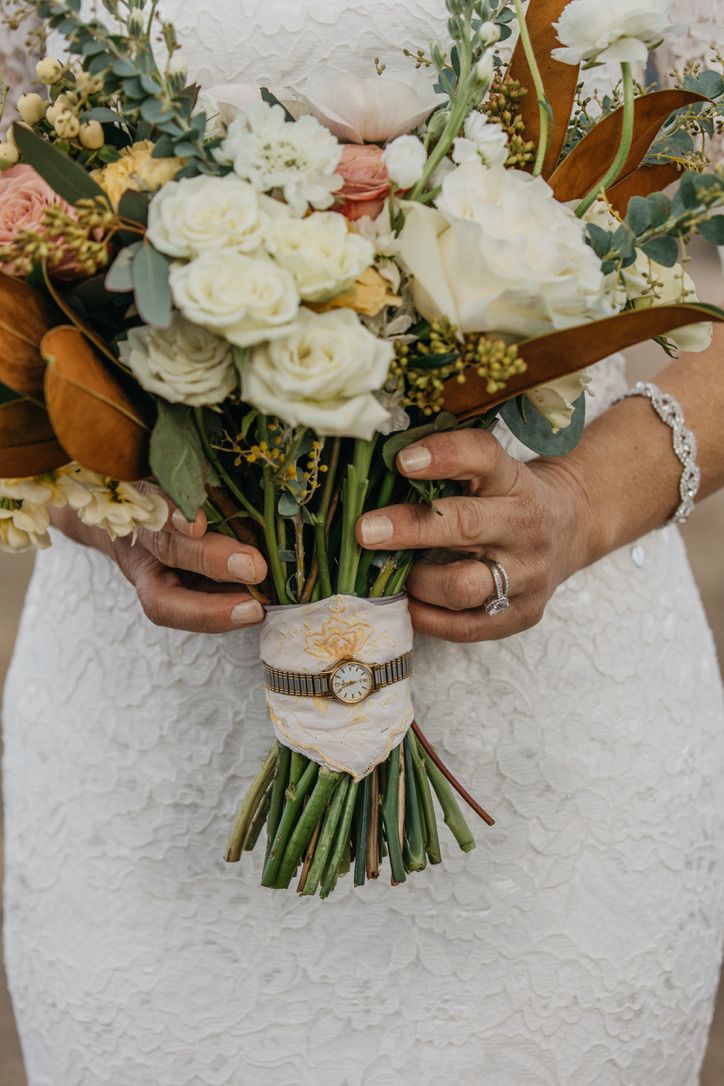 Bridal bouquet of white roses and greenery wrapped with vintage brooch and lace.