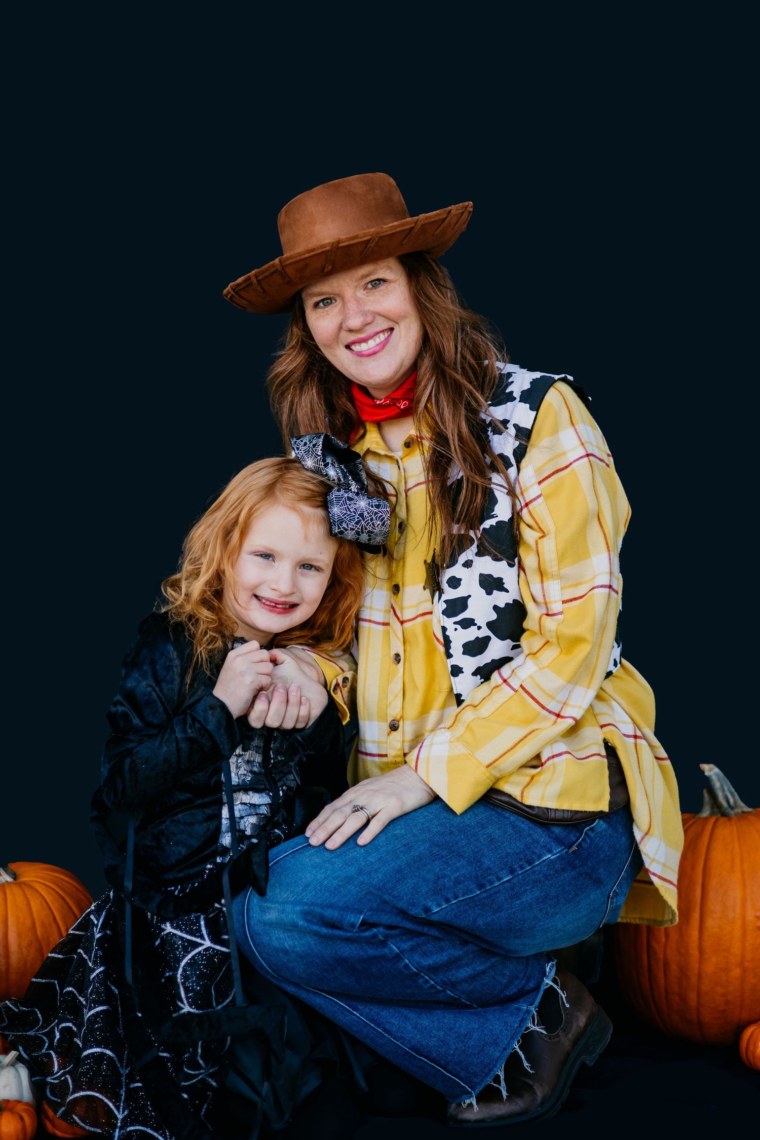 Western-styled portrait with pumpkins and cowboy hat against dark background.