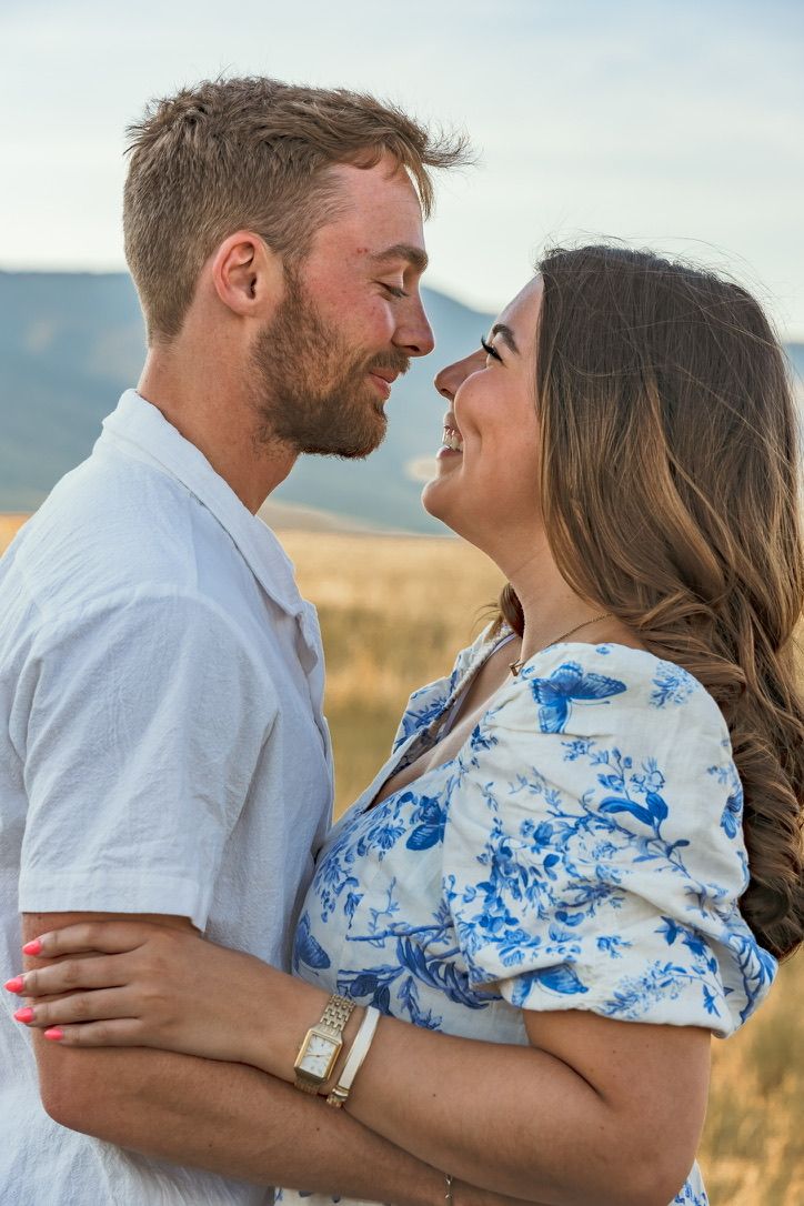A couple in white and blue outfits embraces against a mountainous landscape.