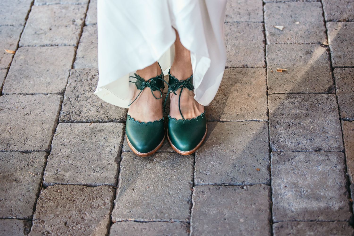 Wedding shoes and dress hems shown against a stone paved floor.