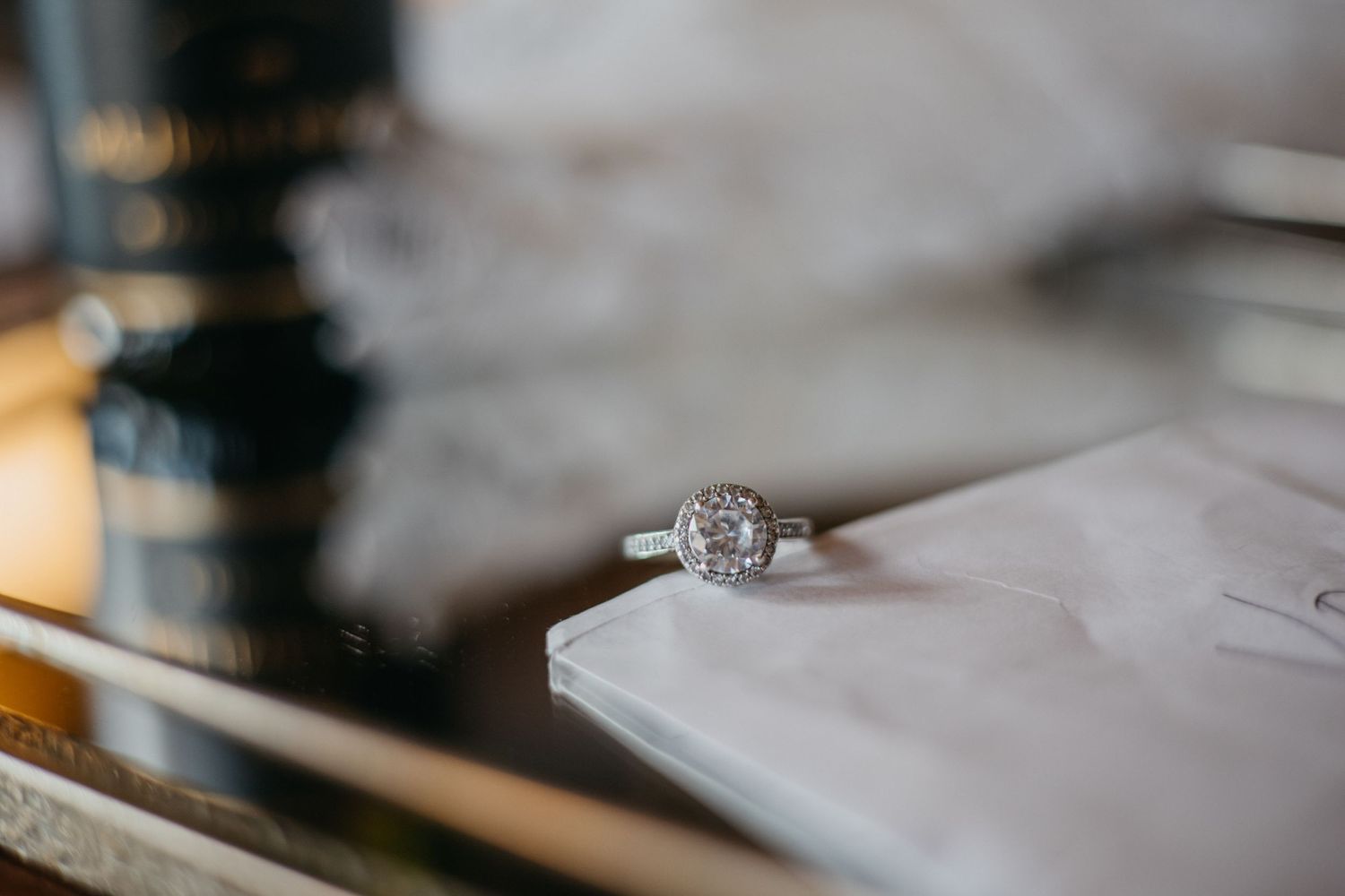 Close-up shot of a diamond engagement ring on a white surface with soft bokeh background.