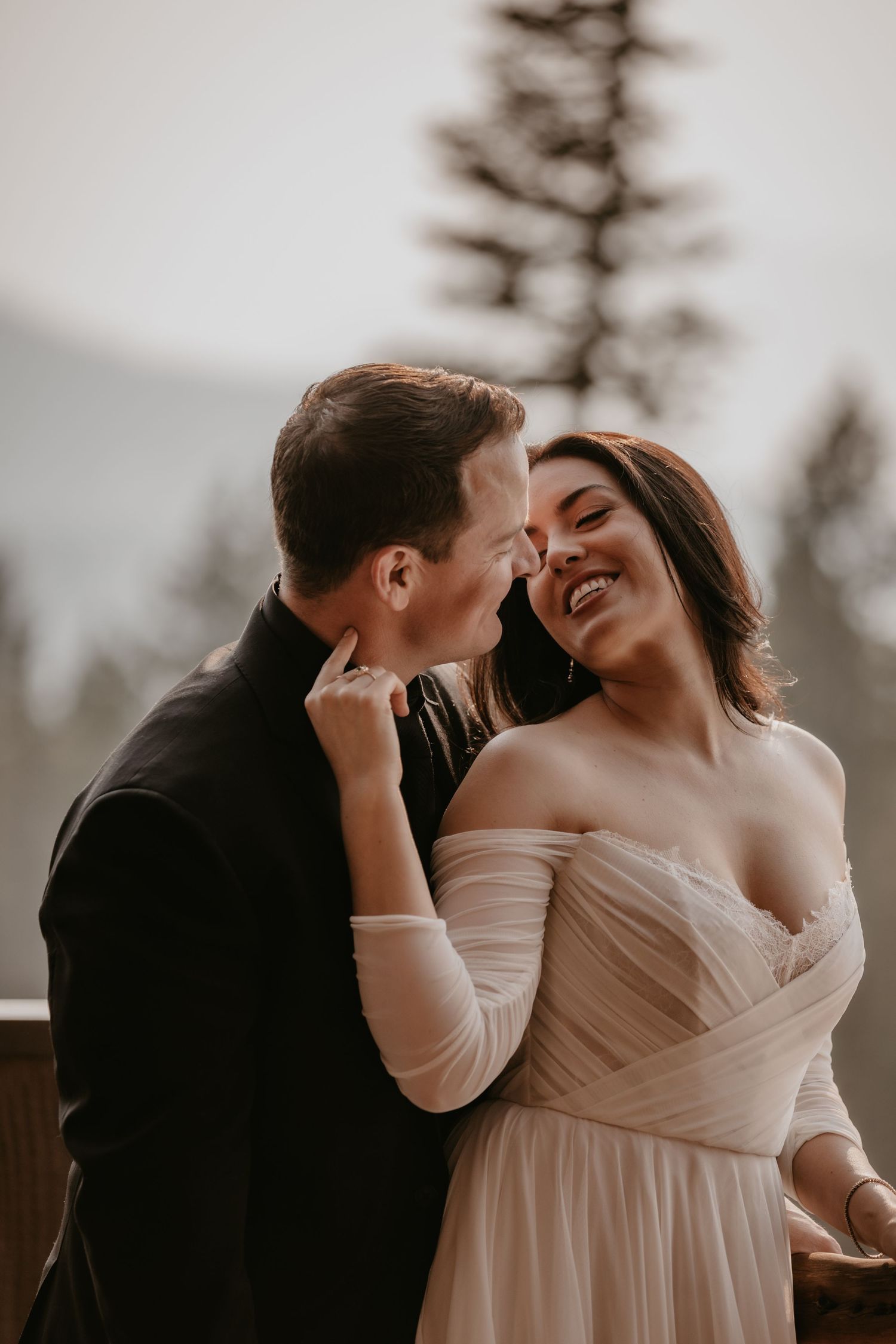 Romantic outdoor wedding portrait against mountain backdrop in soft lighting.
