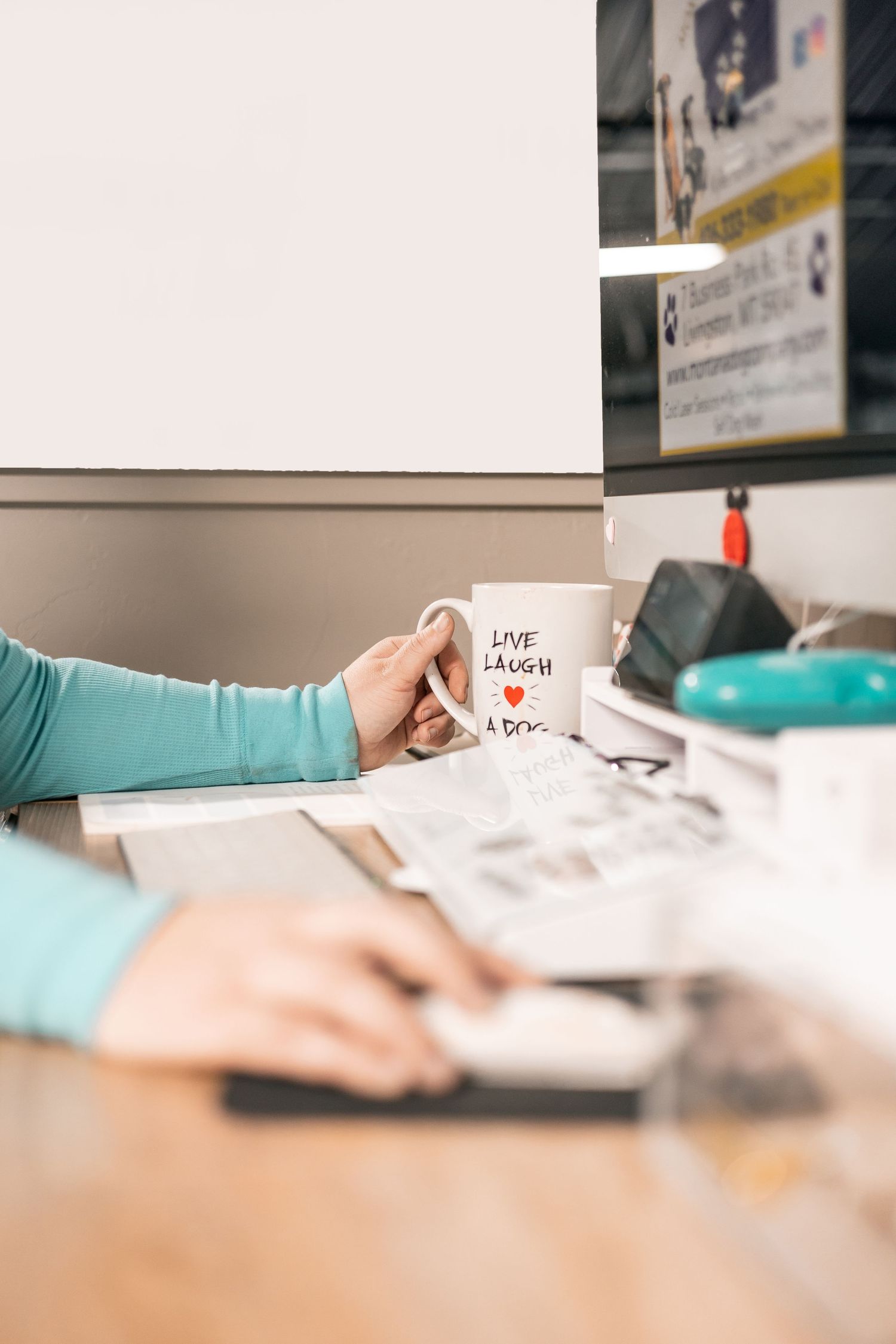 A white coffee mug with a heart design sits on a desk with blurred office supplies in the background.