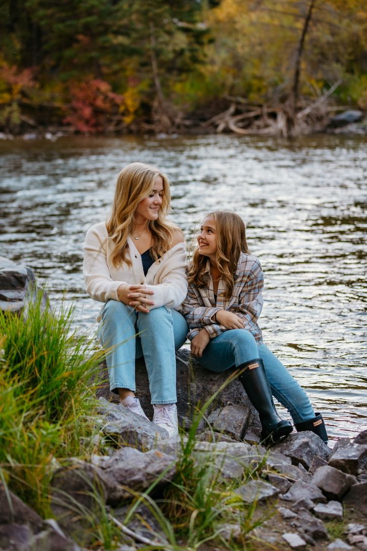 Two people sitting on rocks by a river surrounded by fall foliage.