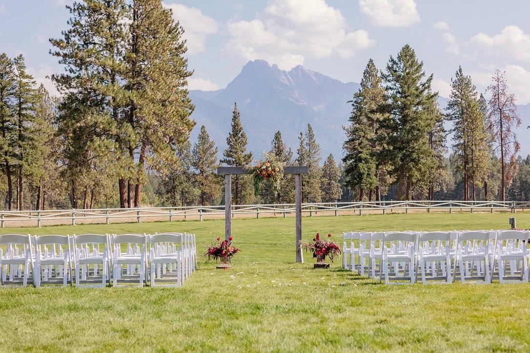 Outdoor wedding ceremony setup with white chairs facing mountain vista through evergreen trees.