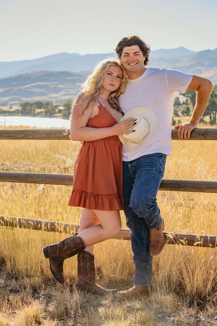 A couple poses romantically against a rustic wooden fence in a golden field.