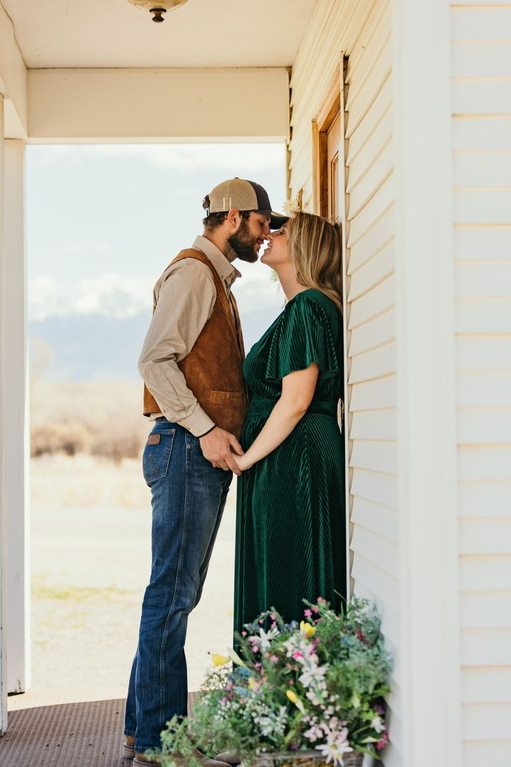 A couple shares a tender moment on a white porch with decorative floral arrangements.